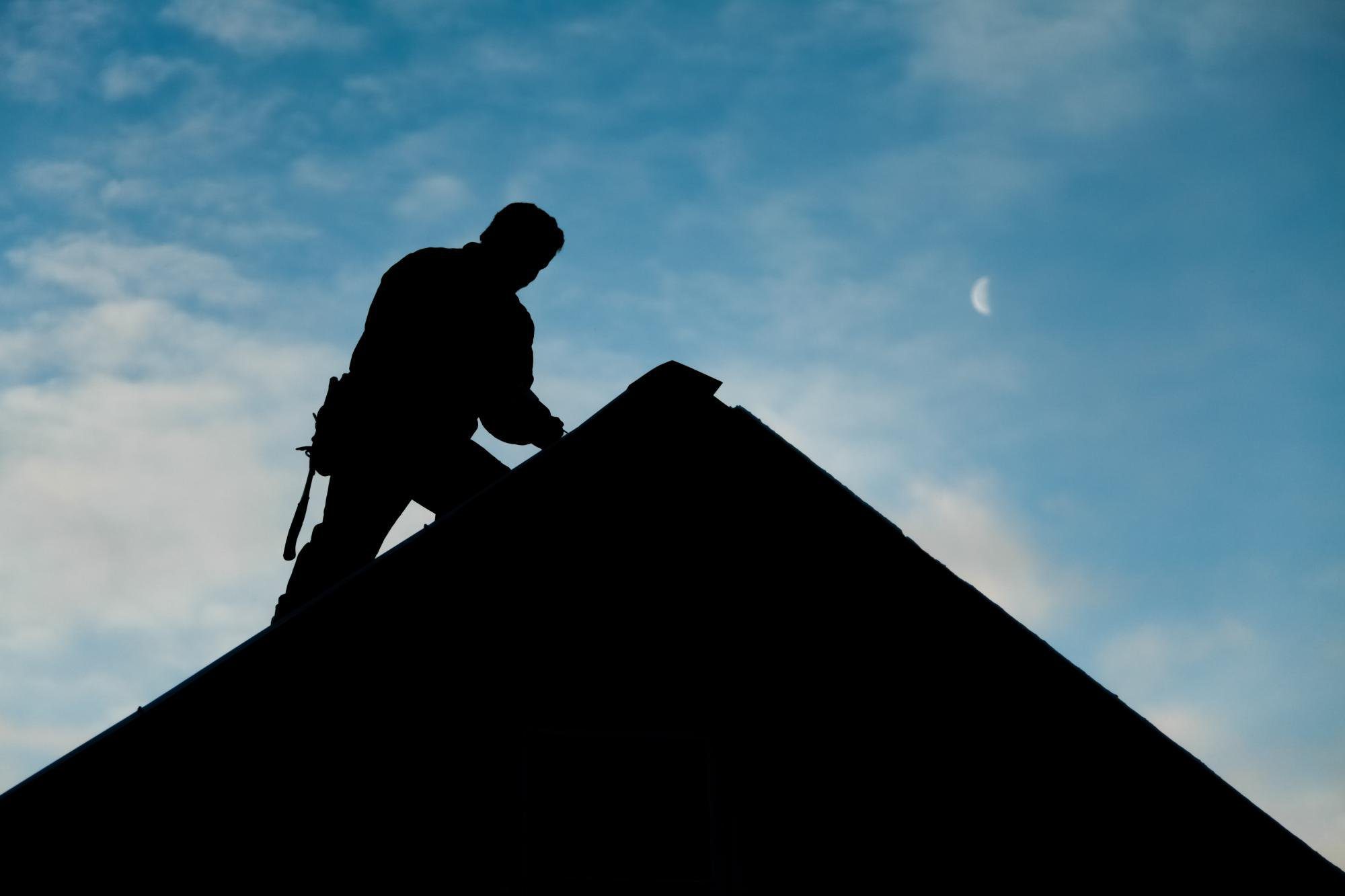 silhouette of a man walking on the roof while performing repairs .
