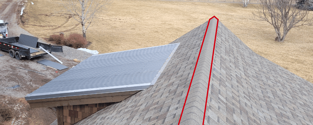 ridge of a shingle roof with red lines indicating where one would install ridge shingles with savannah grass in the background. How to shingle a roof.